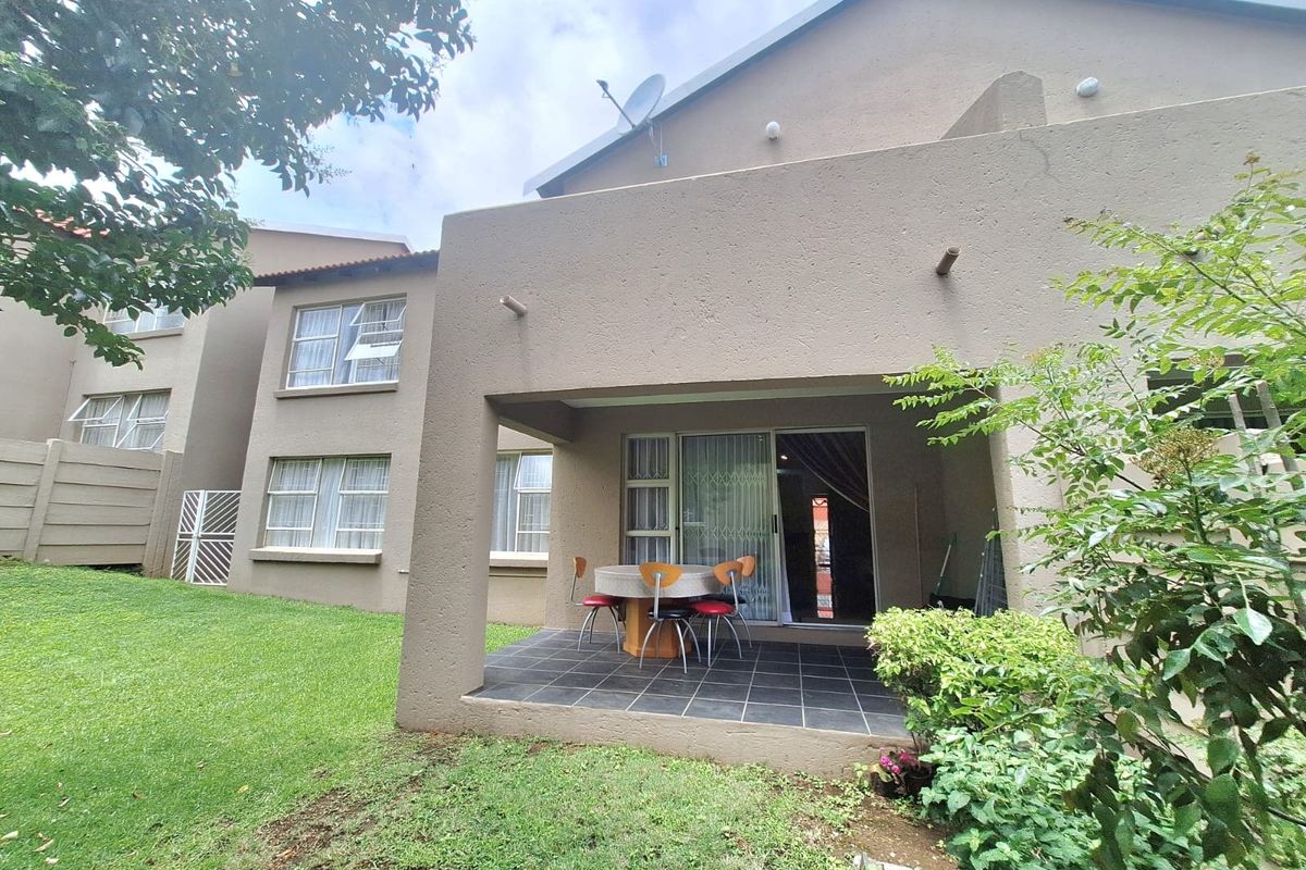 Rear view of the townhouse featuring a covered tiled patio, sliding glass doors, and a private garden area.