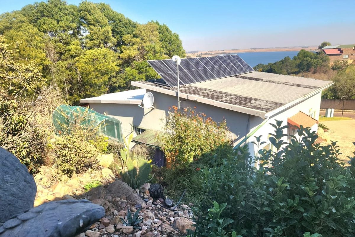 An elevated view of the property roof featuring installed solar panels and a satellite dish, set against a natural landscape and water backdrop.