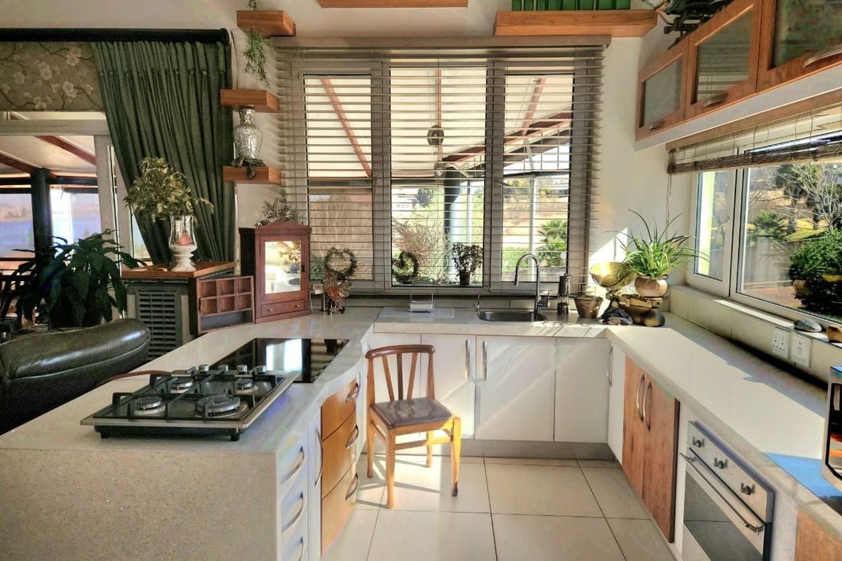 A well-lit kitchen featuring stone countertops, a gas hob, built-in oven, and modern cabinetry with floating shelves and large windows overlooking the garden.