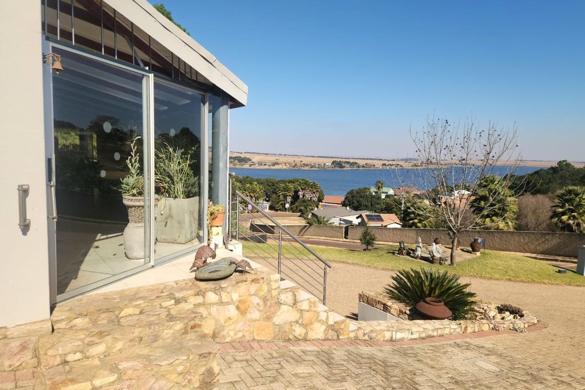 Rear exterior view featuring a stone retaining wall, paved driveway, and a covered patio area with sliding glass doors overlooking the landscape.