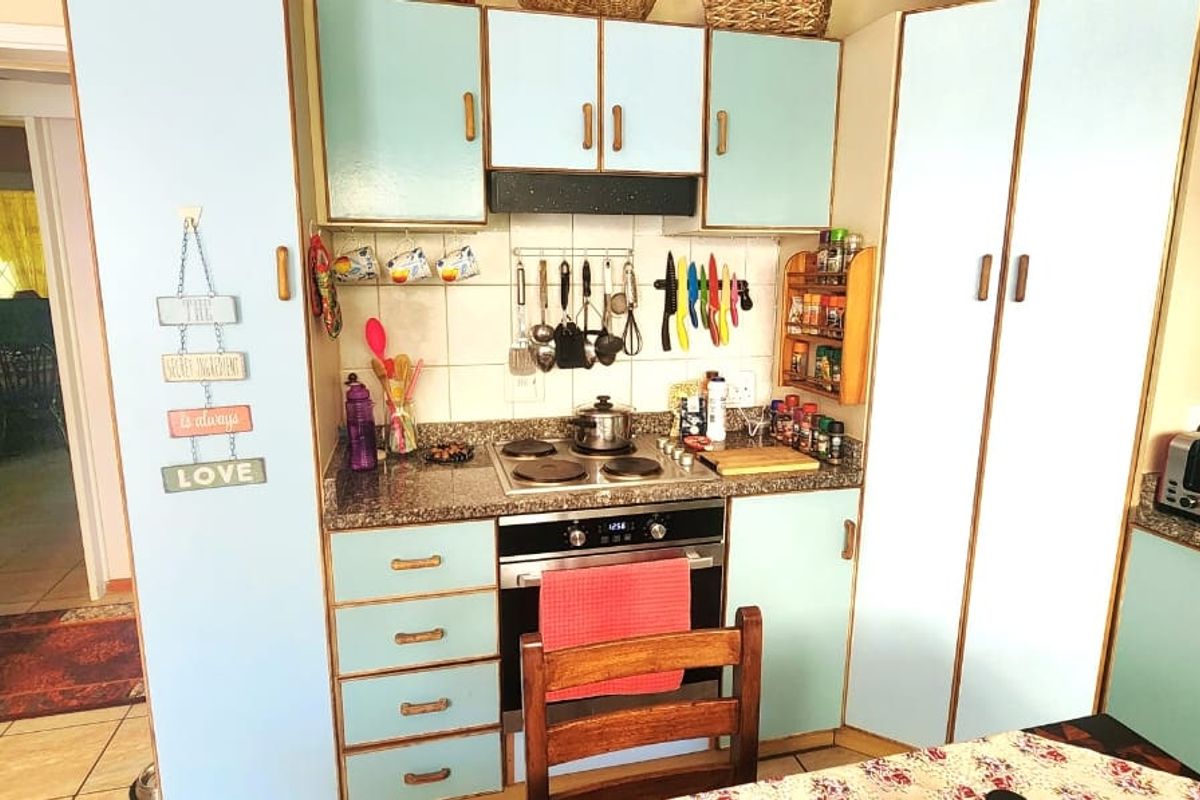 Compact kitchen featuring light blue cabinetry, granite countertops, a built-in oven, and an electric hob with a tiled backsplash.