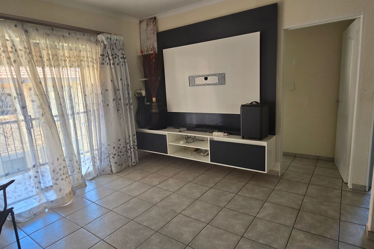 A living room featuring tiled flooring, a built-in media console, and a sliding glass door providing access to the exterior.
