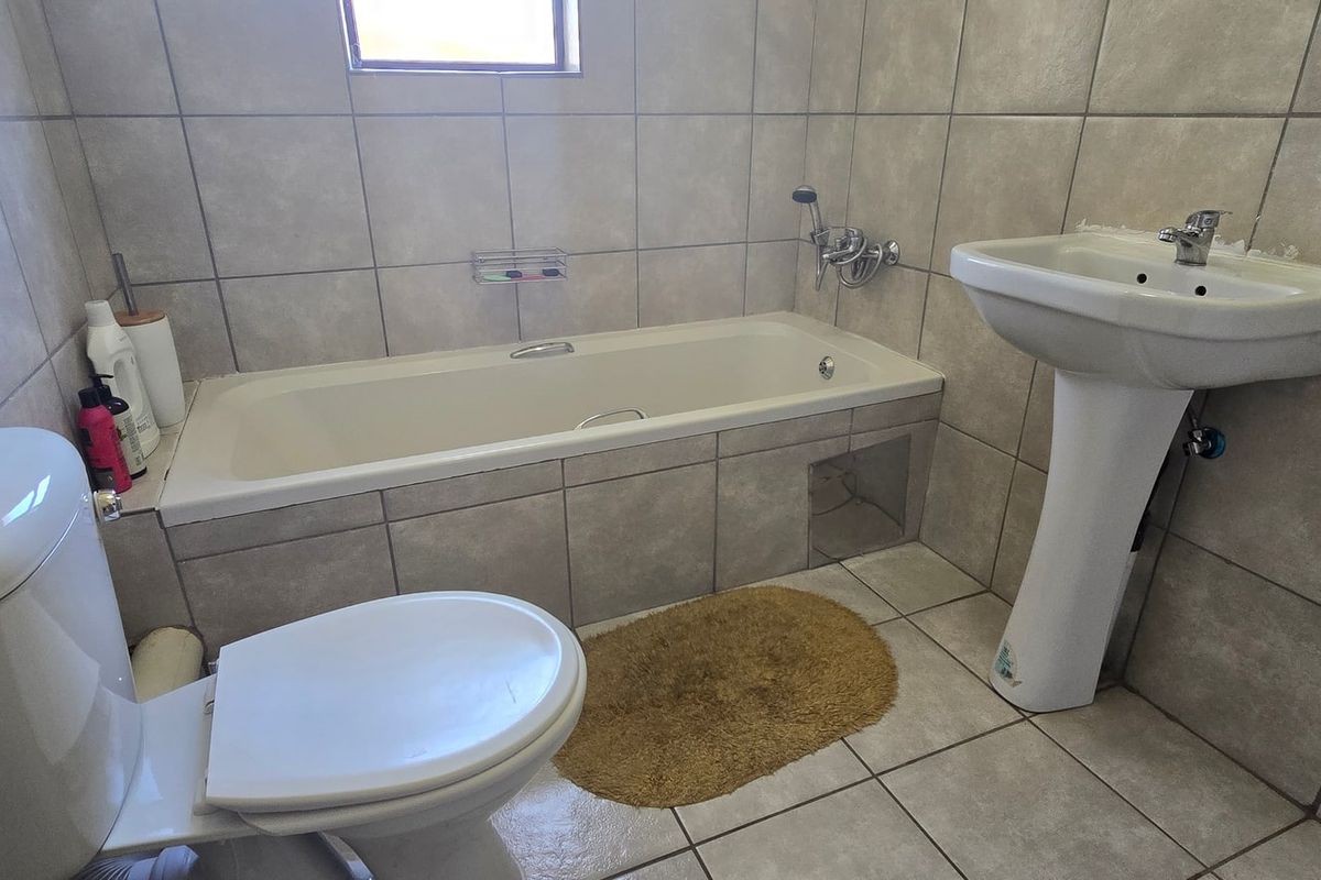 A functional bathroom featuring a pedestal washbasin, built-in bathtub, and toilet with neutral wall and floor tiling.