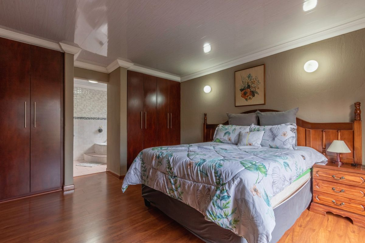 A well-maintained bedroom featuring warm laminate flooring, extensive built-in wooden cabinetry, and an en-suite bathroom access.