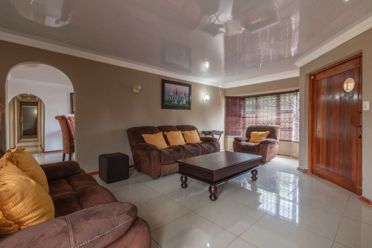 Spacious living room featuring glossy ceiling finish, large bay window with blinds, tiled flooring, and an arched entryway leading to adjacent living areas.