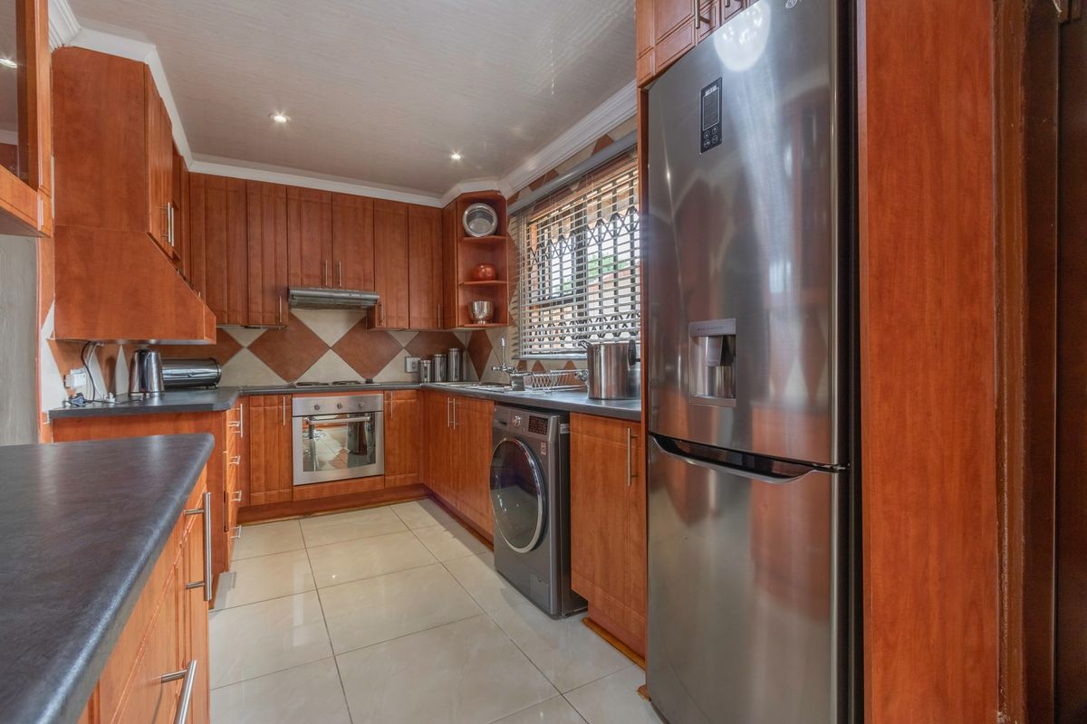 A functional kitchen featuring warm-toned wooden cabinetry, tiled backsplash, integrated oven, and tiled flooring, offering a practical layout for daily meal preparation.