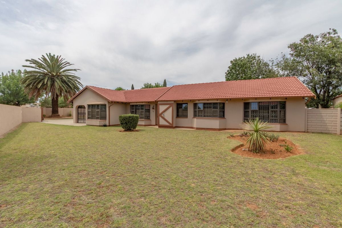 A well-maintained single-story house exterior featuring a tiled roof, security bars on windows, and a spacious rear garden with a paved driveway.