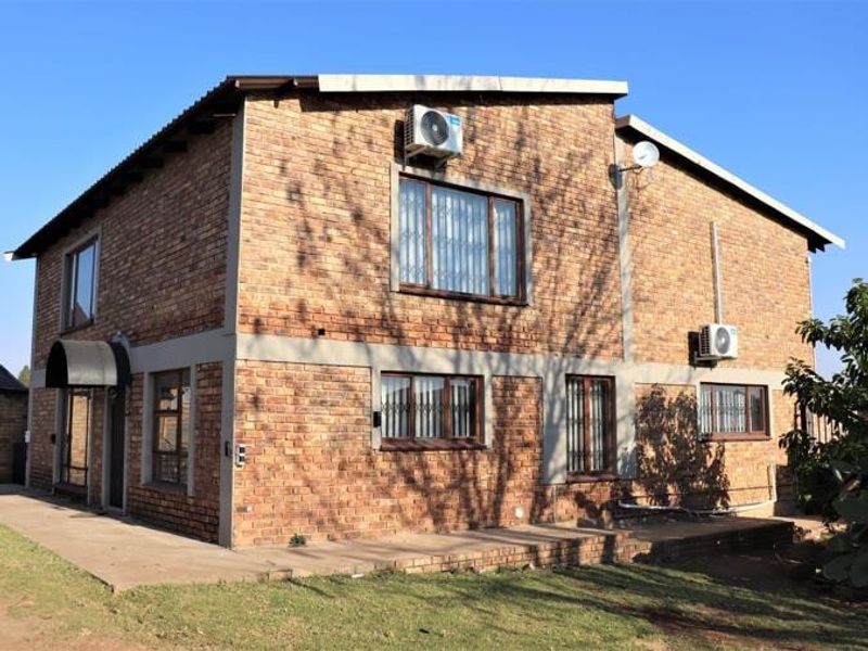 A two-story face-brick farm building featuring multiple air conditioning units, security-barred windows, and a concrete patio area.