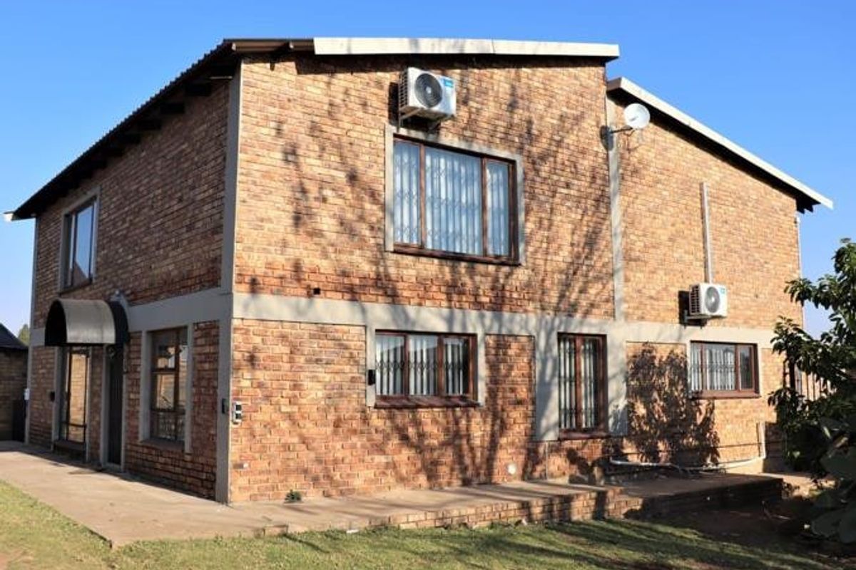 A two-story face-brick farm building featuring multiple air conditioning units, security-barred windows, and a concrete patio area.