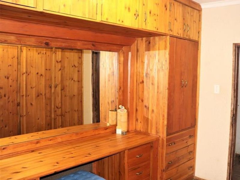 A bedroom featuring extensive built-in wooden cabinetry, including a vanity unit with an integrated mirror and overhead storage cupboards.
