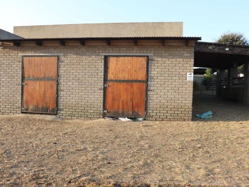 A functional farm utility building featuring brick construction with two timber stable doors and an adjacent covered outdoor area.