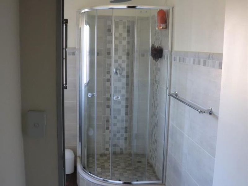 A clean bathroom featuring a curved glass shower enclosure with mosaic tile accents and a wall-mounted towel rail.