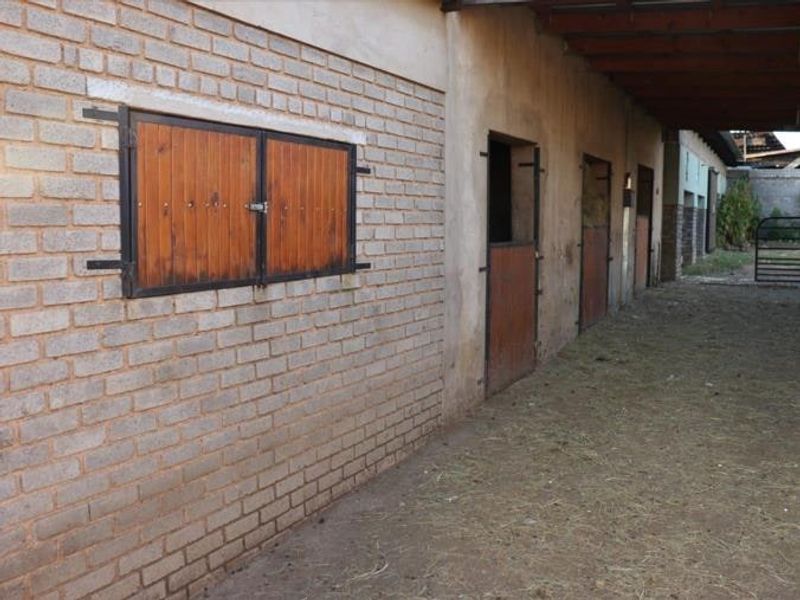 A row of functional horse stables featuring brick construction, timber stable doors, and a covered walkway area.