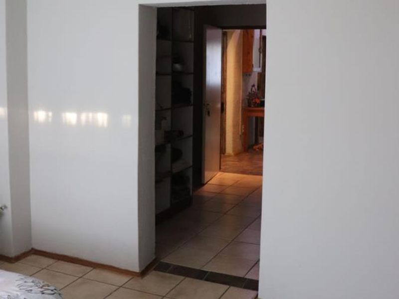 A view through a doorway into a tiled hallway featuring built-in shelving and access to adjacent rooms.