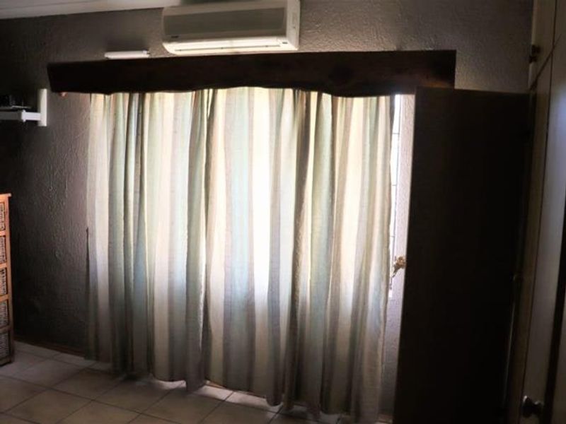 A bedroom featuring tiled flooring, built-in cabinetry, and a wall-mounted split-system air conditioner with a decorative timber pelmet above the window.