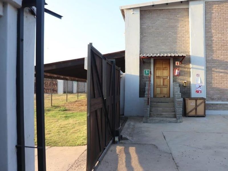 Rear exterior view of a farm building featuring a brick facade, concrete stairs leading to a wooden entrance door, and a metal gate.