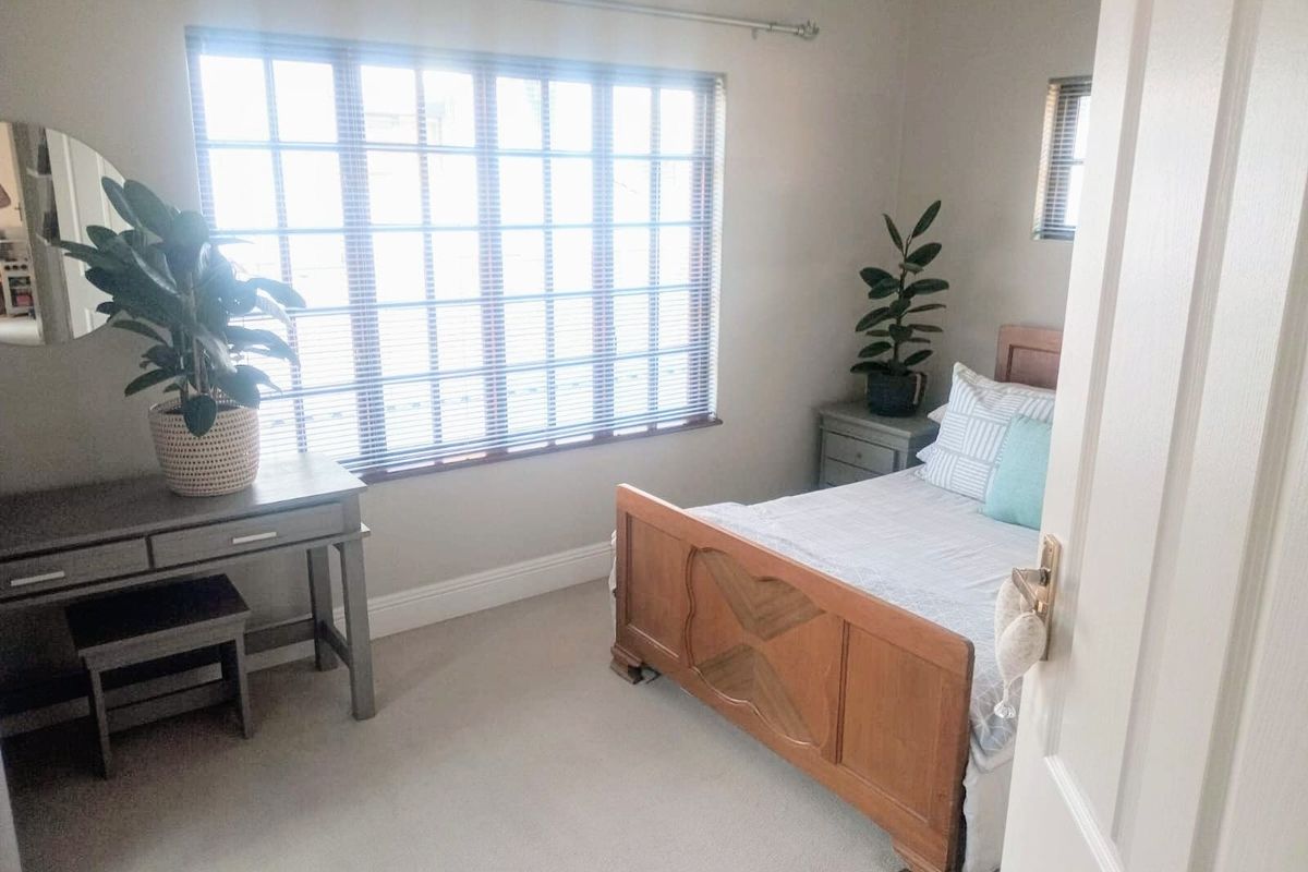 A well-maintained bedroom featuring neutral carpeting, skirting boards, and large windows fitted with venetian blinds and a curtain rod.