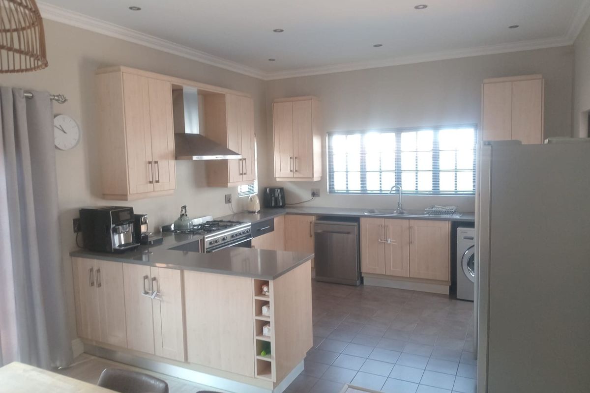 A functional kitchen featuring light wood cabinetry, stone countertops, a gas hob with extractor, and tiled flooring with ample natural light.