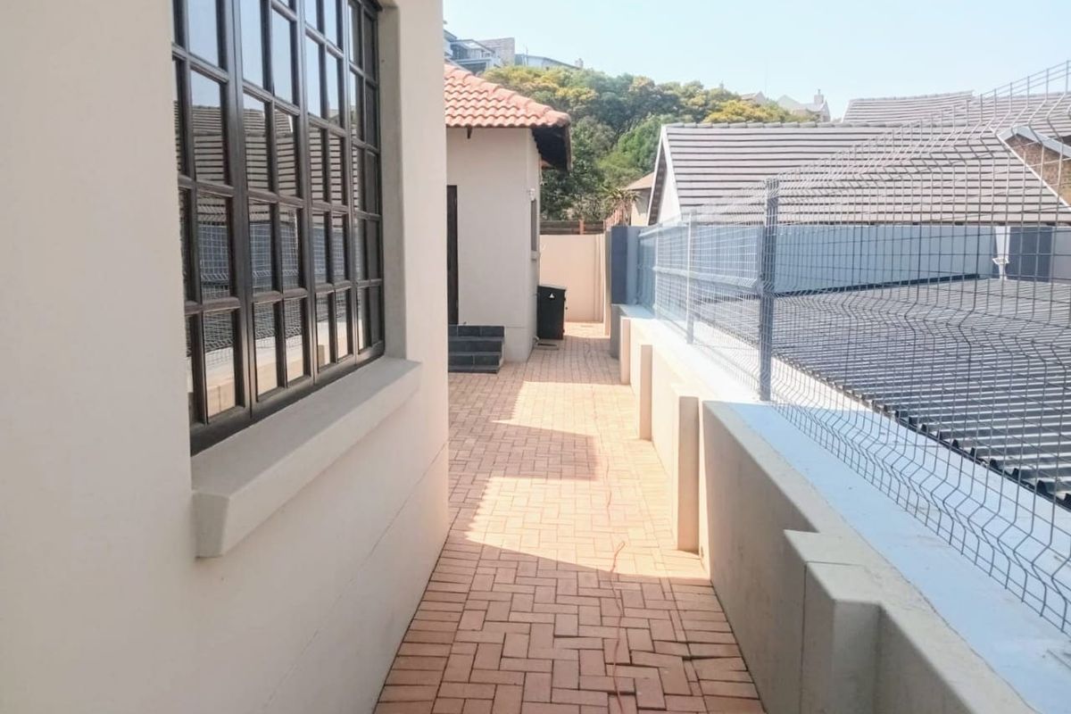 A side exterior walkway featuring paved flooring, security fencing, and views of the adjacent property roofline.