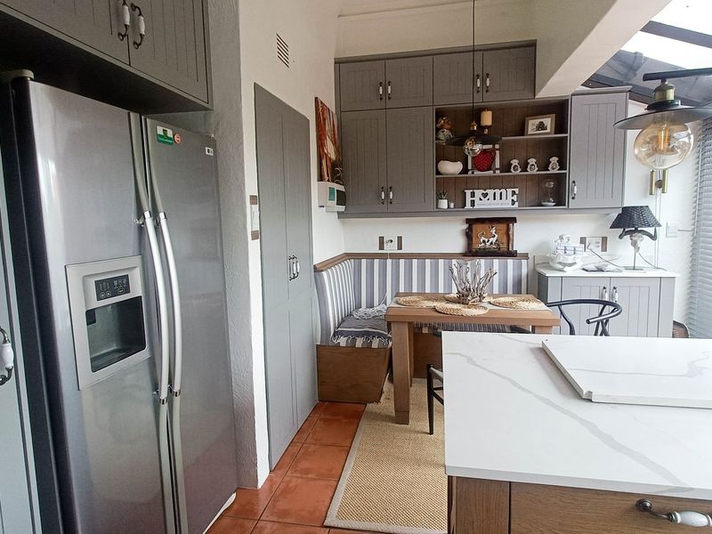 A well-appointed kitchen featuring grey shaker-style cabinetry, stone countertops, a central island, and a cozy built-in dining nook with integrated seating.
