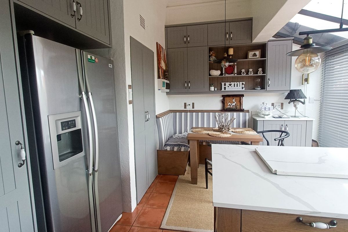 A well-appointed kitchen featuring grey shaker-style cabinetry, stone countertops, a central island, and a cozy built-in dining nook with integrated seating.