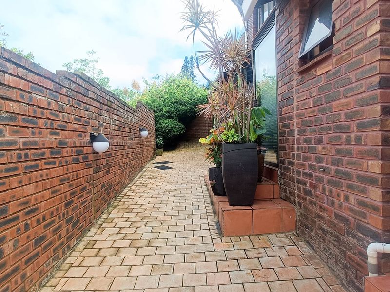 A paved side walkway featuring a brick boundary wall, exterior lighting, and access to the main building structure.