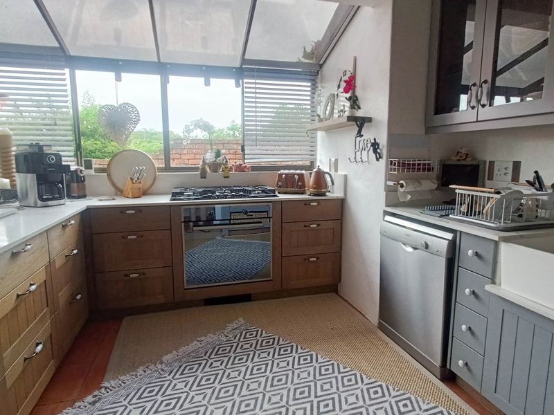 A bright kitchen featuring shaker-style cabinetry, a gas hob, built-in oven, farmhouse sink, and a unique glass roof providing ample natural light.
