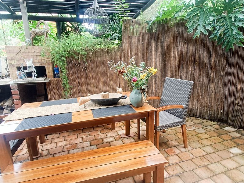 Covered outdoor patio area featuring a built-in brick braai, timber pergola structure, and paved flooring, ideal for alfresco dining and entertaining.
