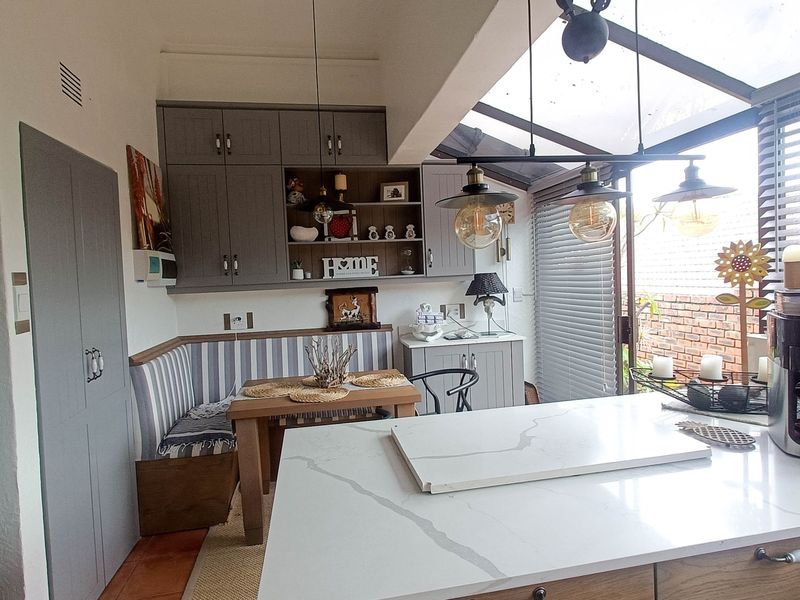 Modern open-plan kitchen area featuring a central island with quartz countertop, built-in cabinetry, and a bright dining nook under a glass roof.