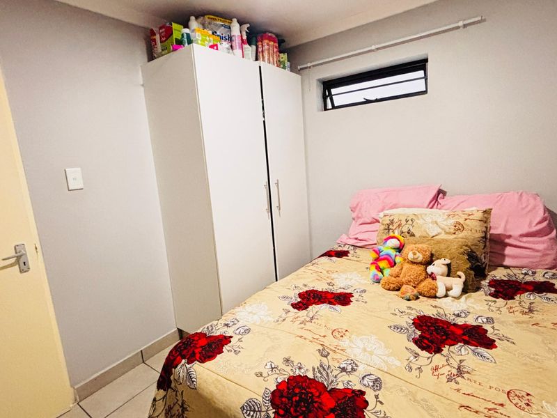 A compact bedroom featuring tiled flooring, a built-in wardrobe, and a small horizontal window for natural light.