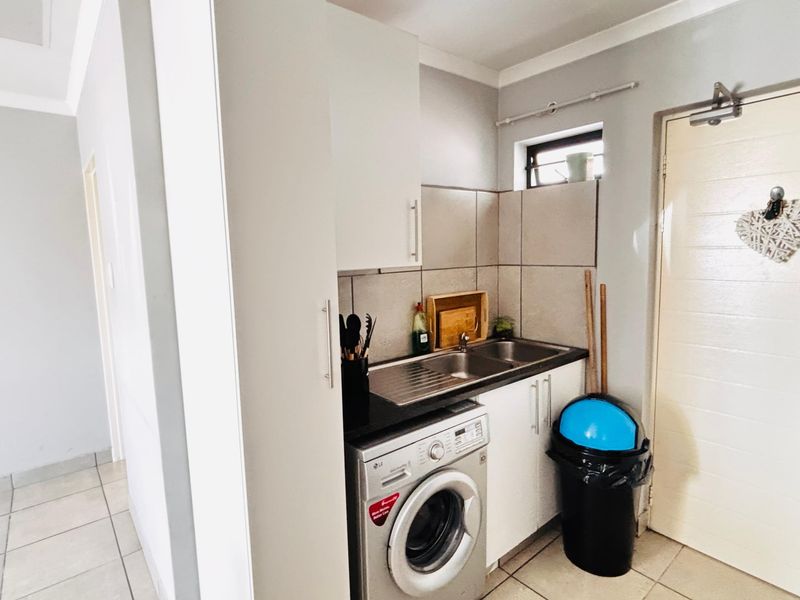 Compact laundry area featuring built-in cabinetry, a stainless steel sink, tiled splashback, and space for a washing machine.