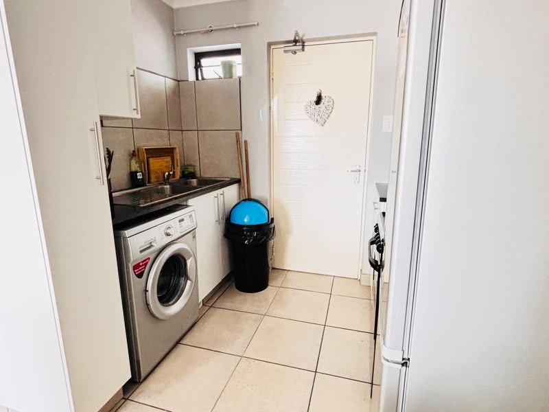 A functional laundry area featuring tiled flooring, built-in cabinetry, a stainless steel sink, and a secure door with a hydraulic closer.