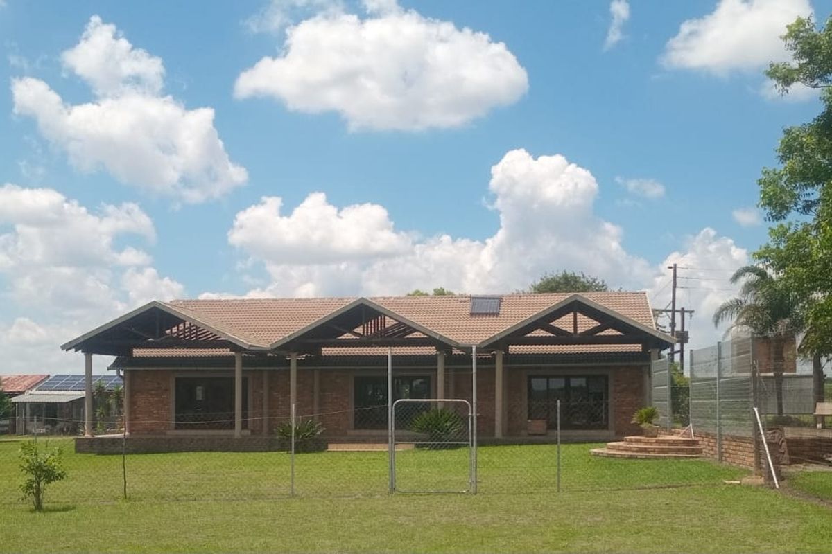 A spacious farm-style residence featuring a multi-gabled tiled roof, brick facade, and a wide covered patio overlooking a large, well-maintained garden.