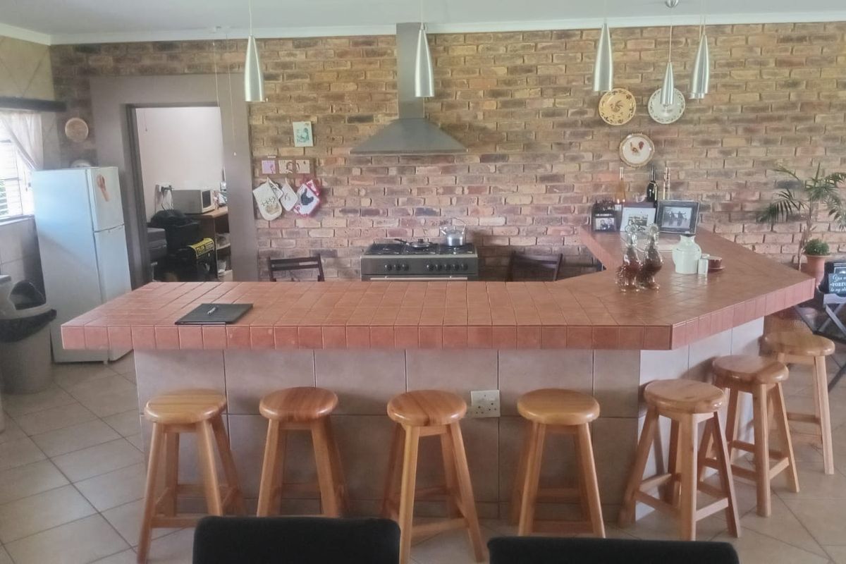 Spacious kitchen featuring a large tiled breakfast bar, exposed brick feature wall, stainless steel extractor fan, and a gas stove.