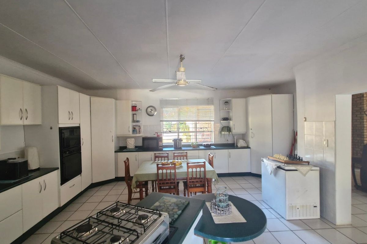 Spacious kitchen featuring white cabinetry, dark countertops, a gas hob, built-in oven, and tiled flooring with an integrated dining area.
