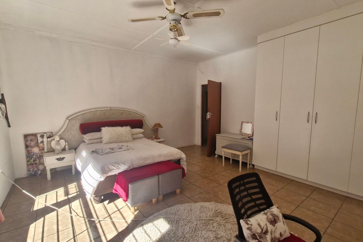 A spacious bedroom featuring tiled flooring, a ceiling fan, and ample built-in cupboard storage.