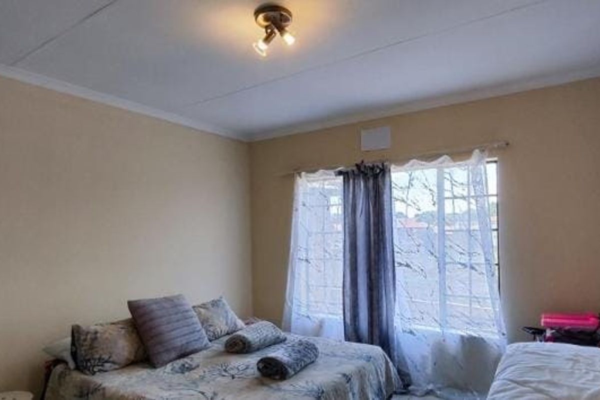 A functional bedroom featuring a window with security bars and a central ceiling light fixture, providing a neutral space ready for personalization.