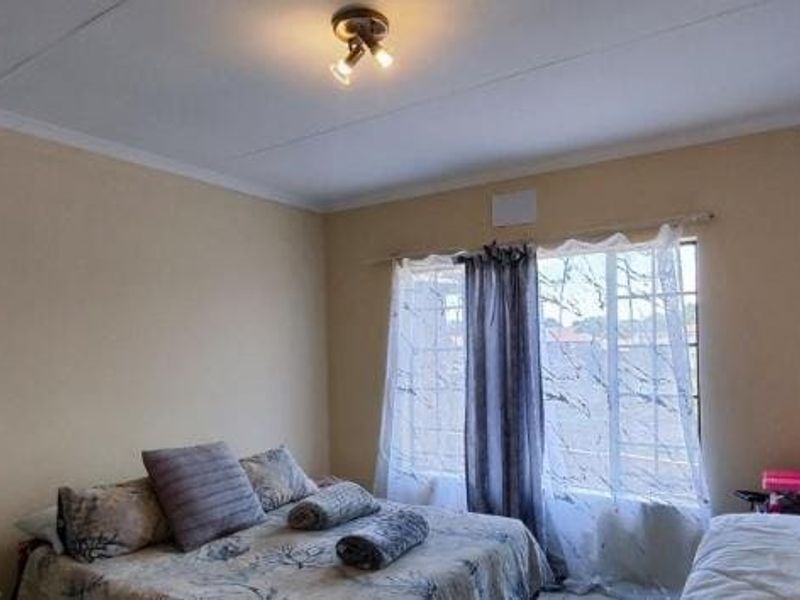 A functional bedroom featuring a window with security bars and a central ceiling light fixture, providing a neutral space ready for personalization.