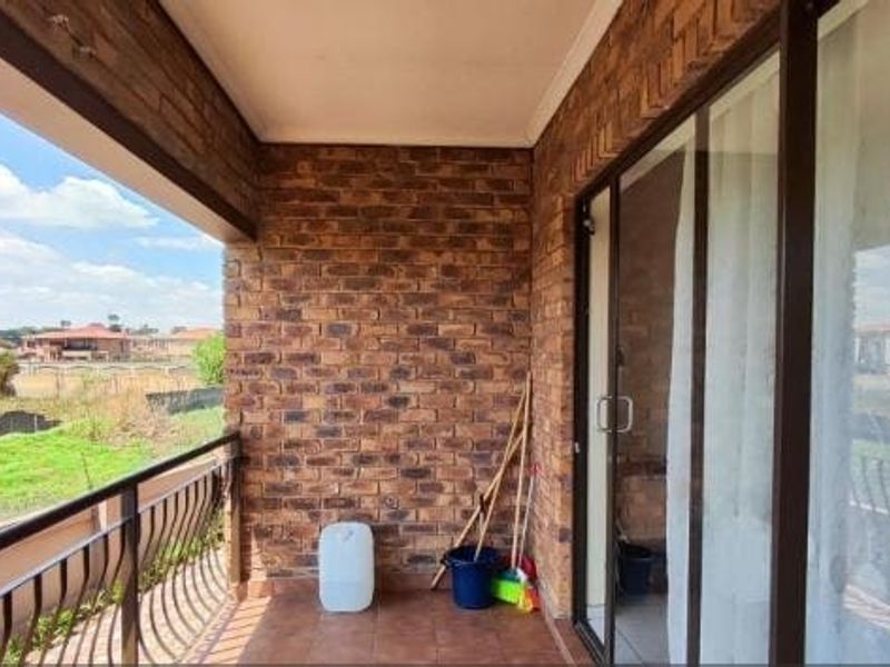 A covered balcony featuring exposed brick walls, tiled flooring, and a metal balustrade, offering an open outdoor space with neighborhood views.
