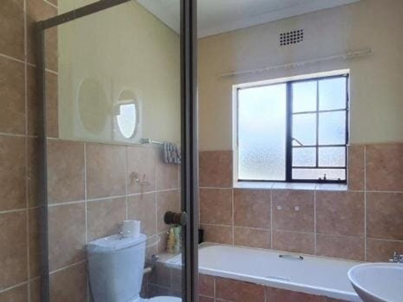 A functional bathroom featuring a bathtub, separate shower enclosure, toilet, and washbasin with neutral wall tiling.