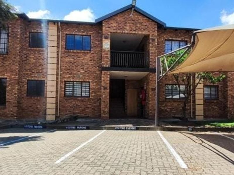 Exterior view of a face brick apartment complex featuring a paved visitors parking area and a shade cloth carport structure.