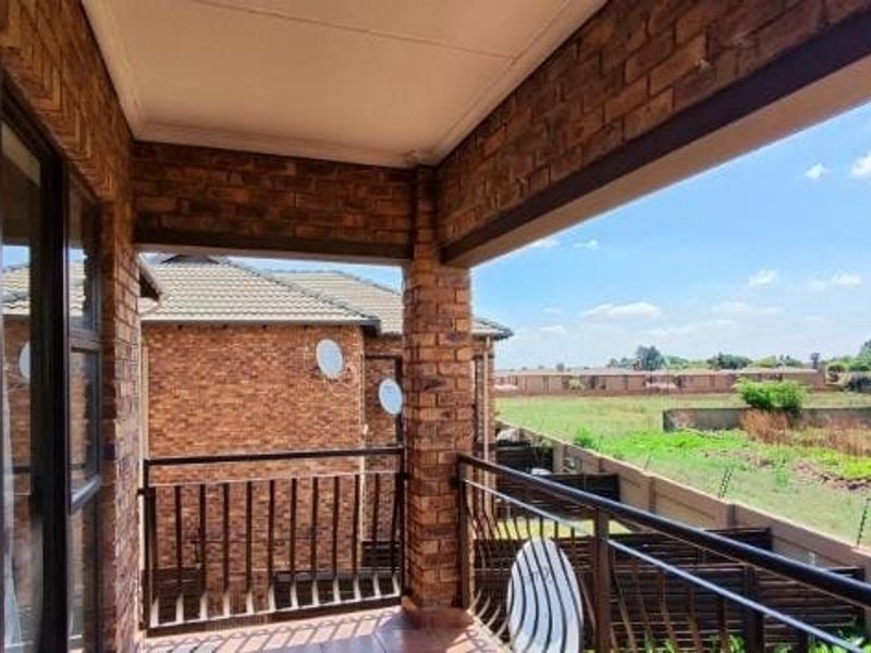 A covered balcony featuring exposed brickwork, metal railings, and tiled flooring, offering an open view of the surrounding neighborhood.