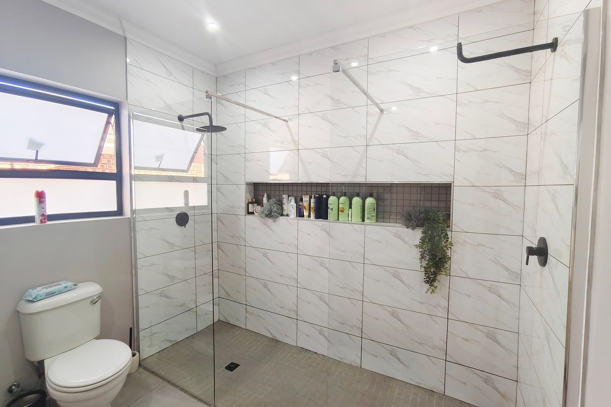 Modern bathroom featuring a spacious walk-in shower with dual shower heads, marble-look wall tiles, a recessed niche, and a contemporary toilet.