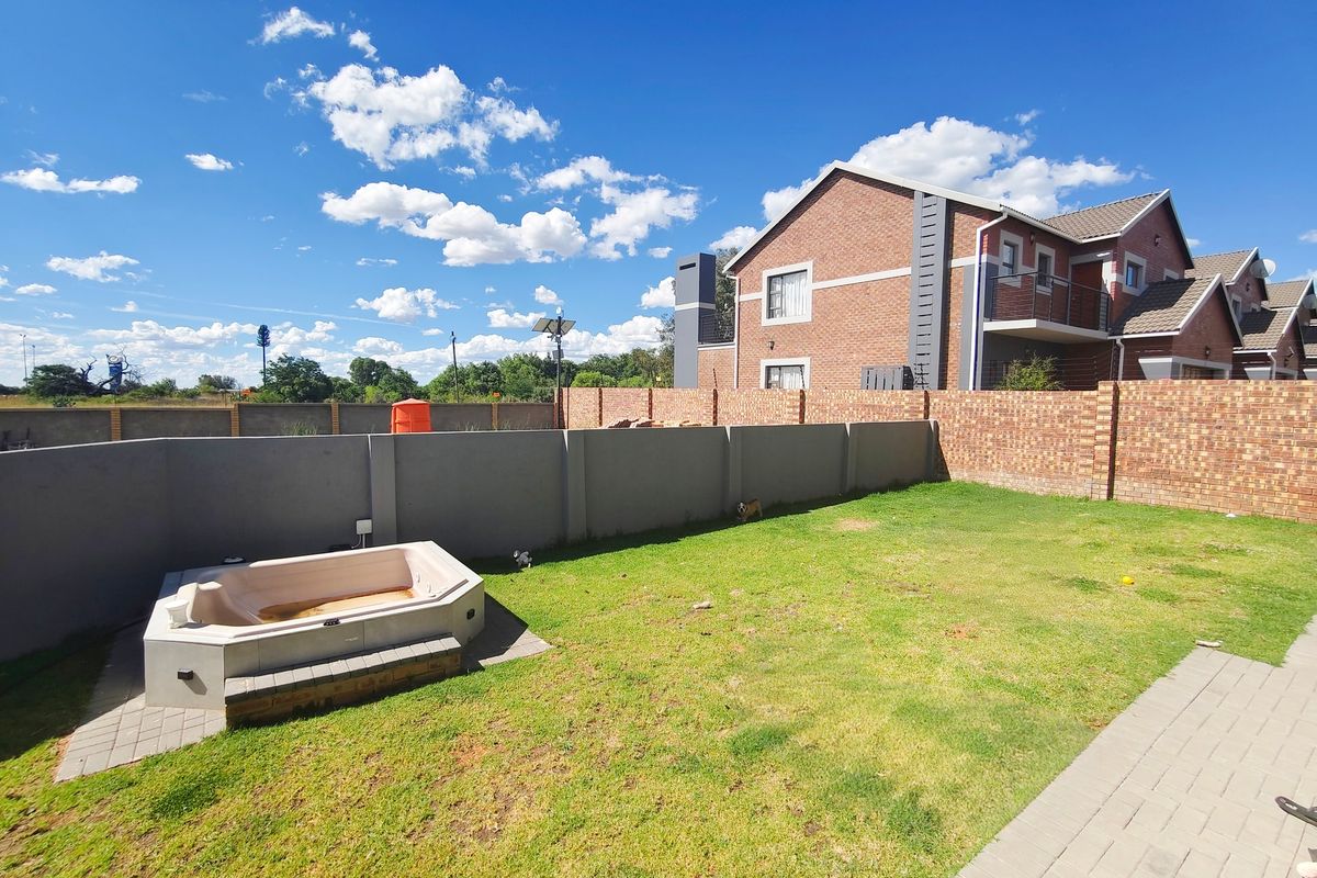 Rear garden area featuring a lawn, paved walkway, and a built-in spa bath, enclosed by brick and plastered boundary walls.