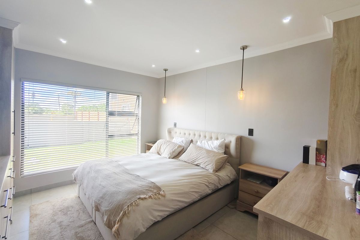 A well-maintained bedroom featuring tiled flooring, recessed downlighting, pendant lights, and built-in cabinetry with large windows fitted with venetian blinds.
