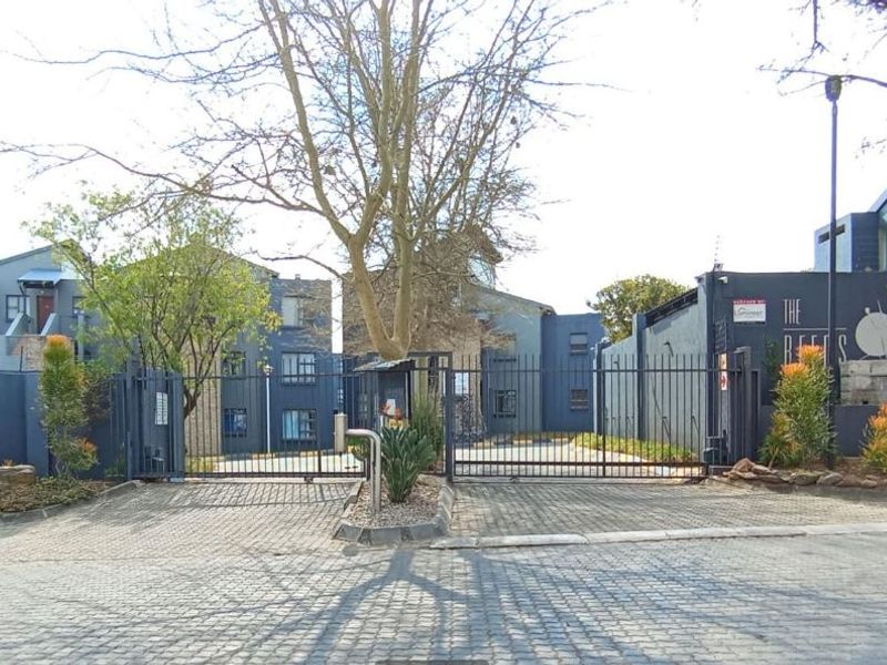 Front entrance view of The Reeds apartment complex featuring secure gated access, paved driveway, and perimeter wall with electric fencing.
