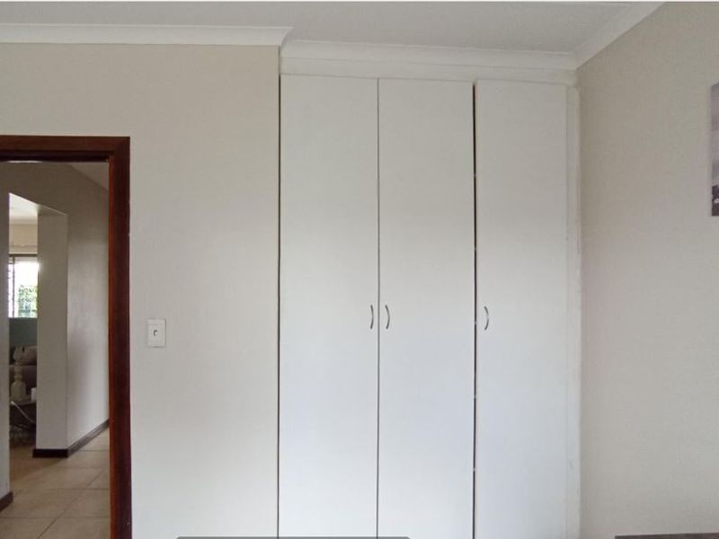 A bedroom featuring built-in white wardrobes and simple cove cornicing, with a doorway leading to an adjacent hallway.