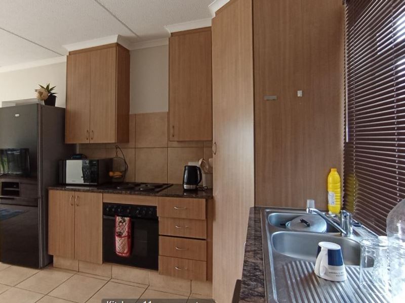 Functional kitchen featuring wood-look laminate cabinetry, dark countertops, built-in oven with hob, and a double bowl stainless steel sink with tiled backsplash.