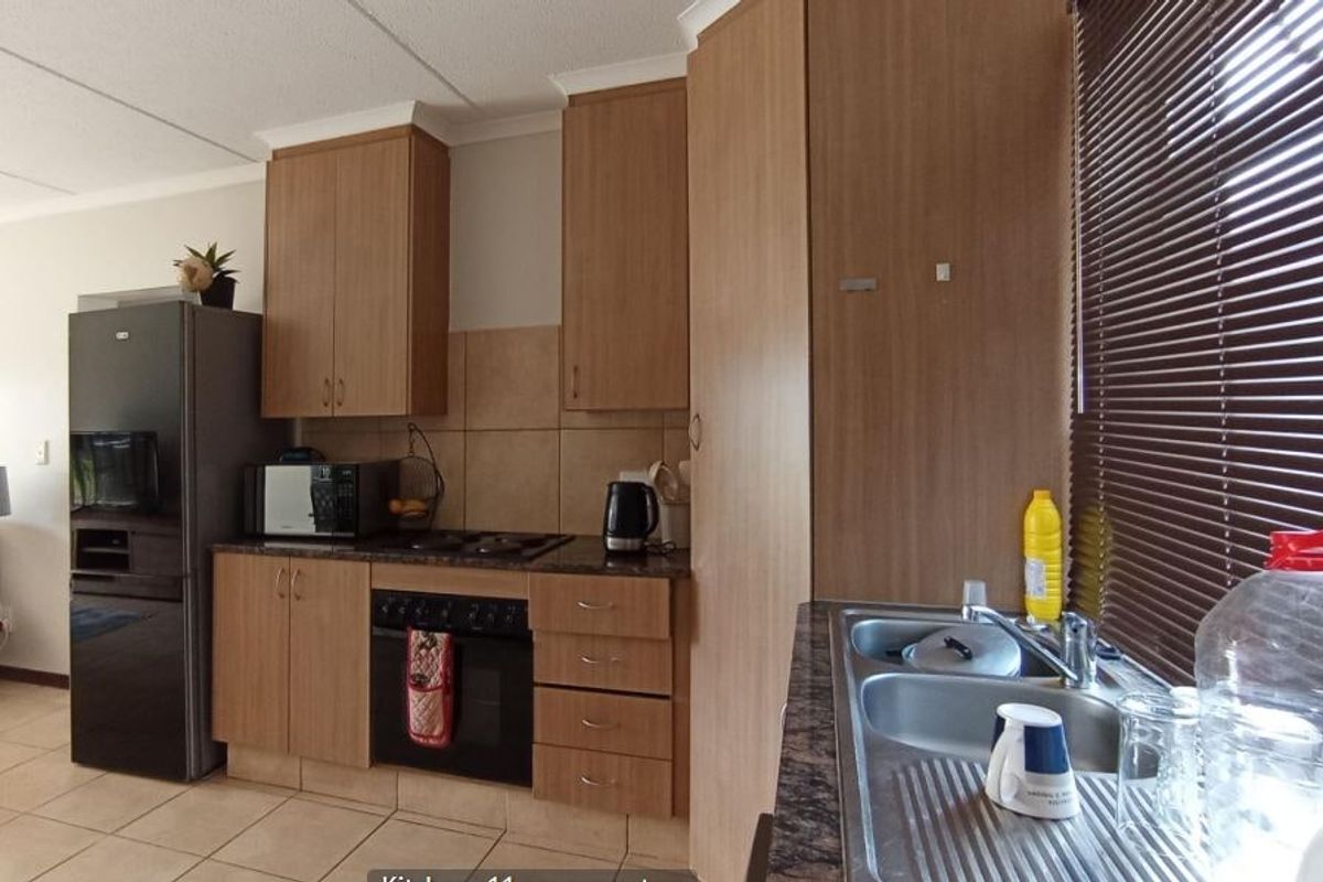 Functional kitchen featuring wood-look laminate cabinetry, dark countertops, built-in oven with hob, and a double bowl stainless steel sink with tiled backsplash.