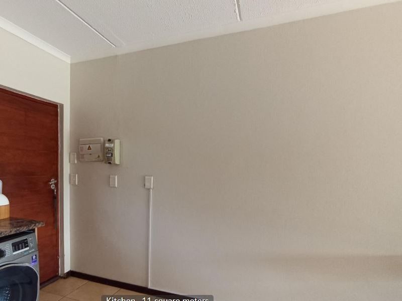 A functional kitchen area featuring tiled flooring, a timber door, and integrated electrical infrastructure including a distribution board and intercom system.